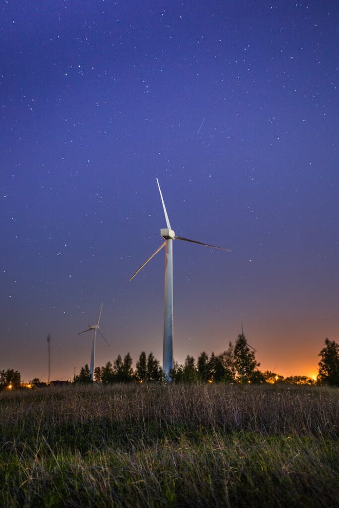 Wind turbines in a grass field under a starry night sky, showcasing renewable energy and sustainability.