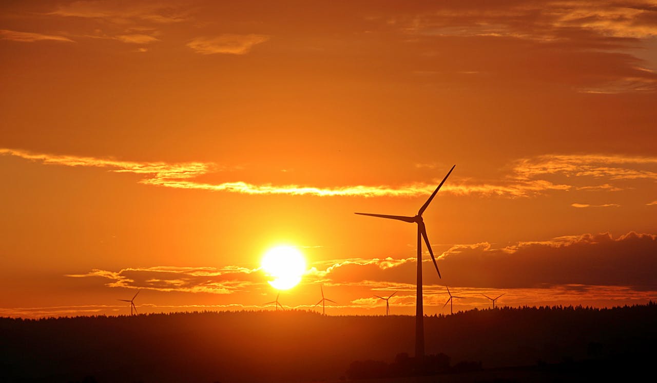 Stunning sunset with silhouetted wind turbines, highlighting renewable energy in a serene landscape.